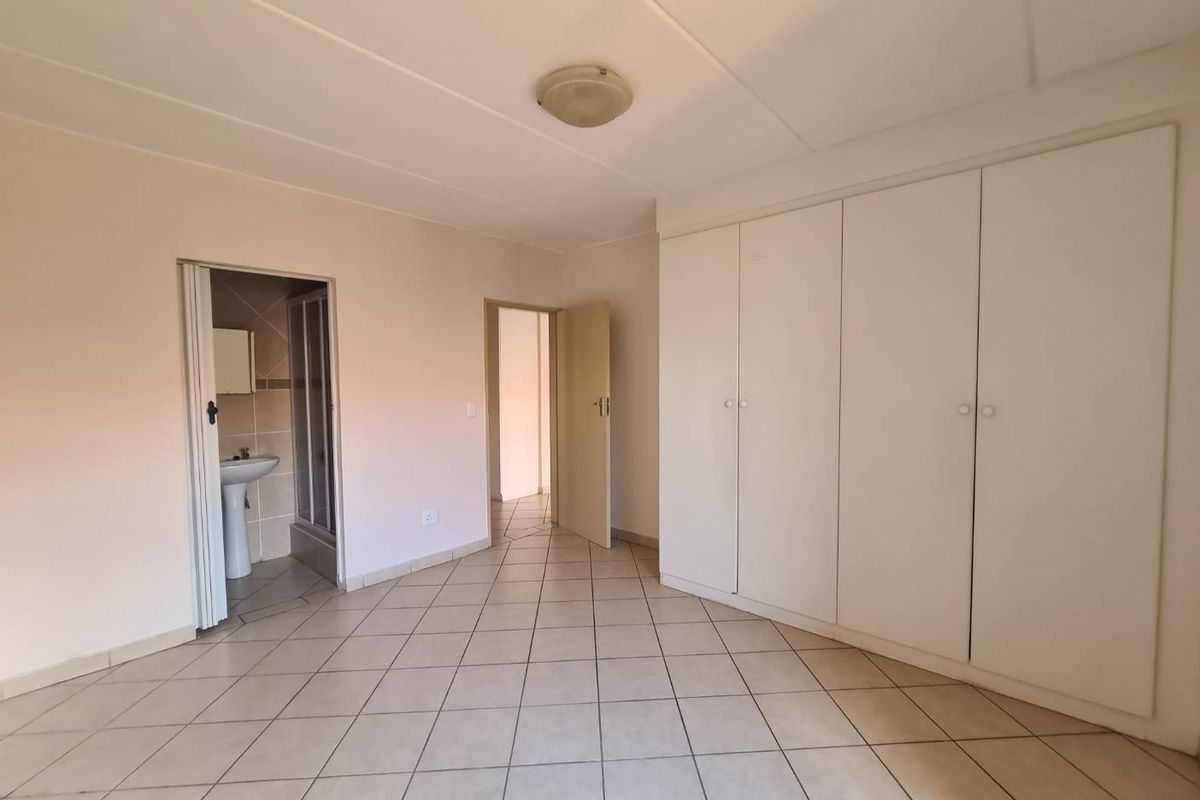 A spacious, empty bedroom featuring neutral tiled flooring, ample built-in cupboard storage, and direct access to an en-suite bathroom.