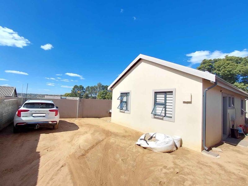 Rear exterior view of the property featuring a plain facade, casement windows with security bars, and an unpaved yard area.