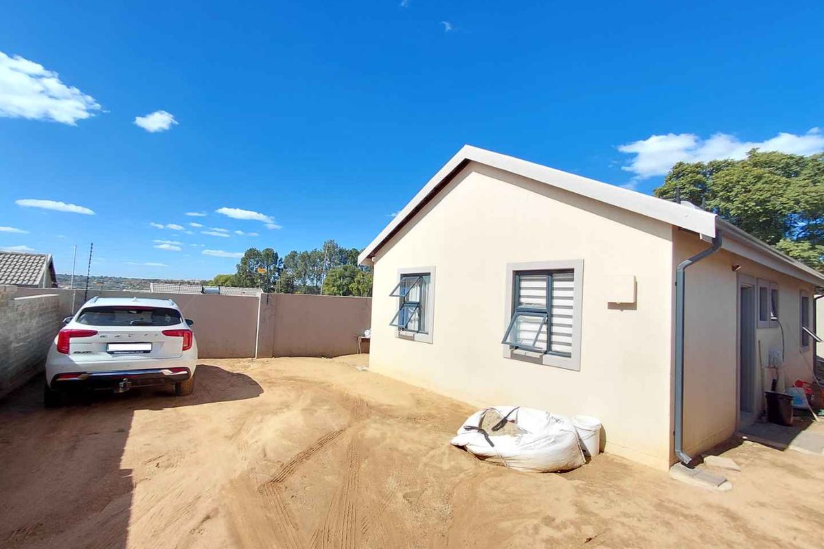 Rear exterior view of the property featuring a plain facade, casement windows with security bars, and an unpaved yard area.