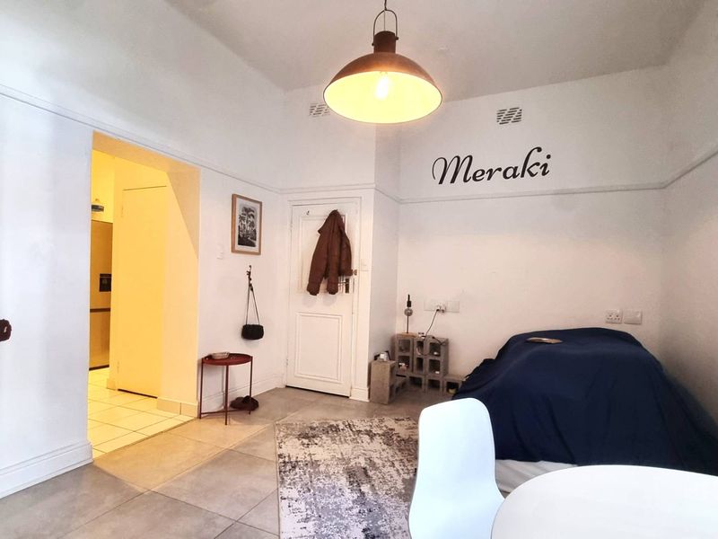 A living area featuring tiled flooring, neutral walls, and a central pendant light, with an adjacent doorway leading to a secondary space.