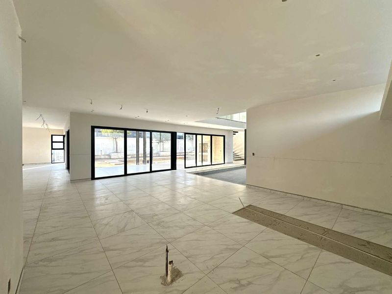 Spacious open-plan living area featuring large format marble-look floor tiles, black aluminium sliding doors, and an unfinished interior awaiting final completion.