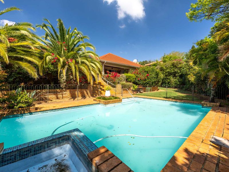 A private outdoor pool area featuring brick paving, established garden landscaping, and a fenced perimeter, set against the rear elevation of the house.