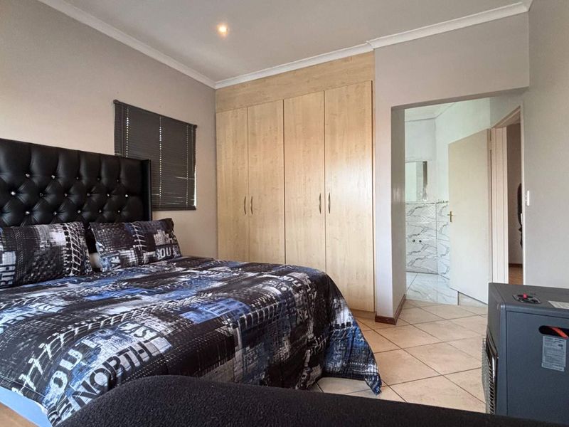 A well-maintained bedroom featuring built-in wooden cupboards, tiled flooring, and direct access to an en-suite bathroom.