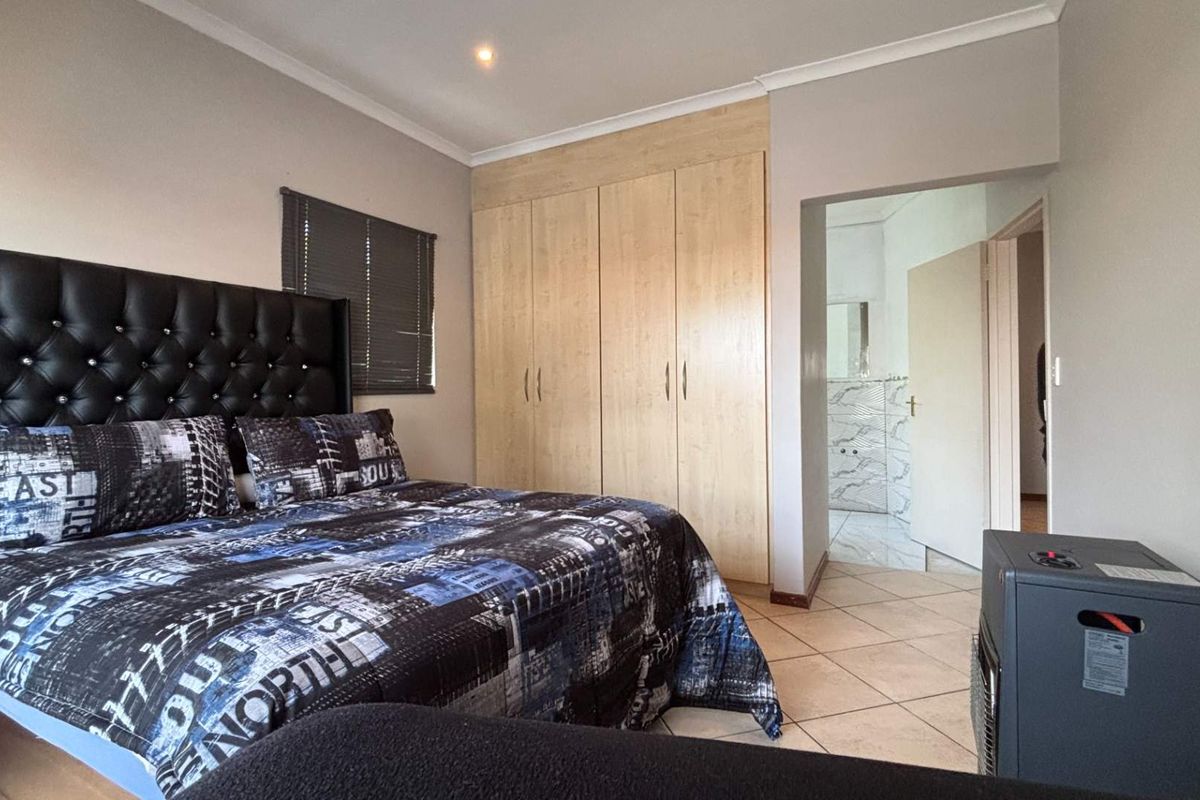 A well-maintained bedroom featuring built-in wooden cupboards, tiled flooring, and direct access to an en-suite bathroom.