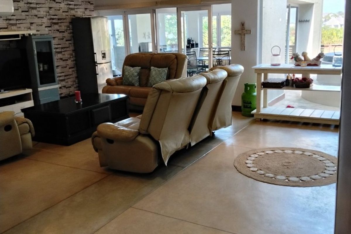 Spacious living area featuring polished concrete floors, a textured stone-cladding feature wall, recessed lighting, and large sliding glass doors leading to an outdoor patio.