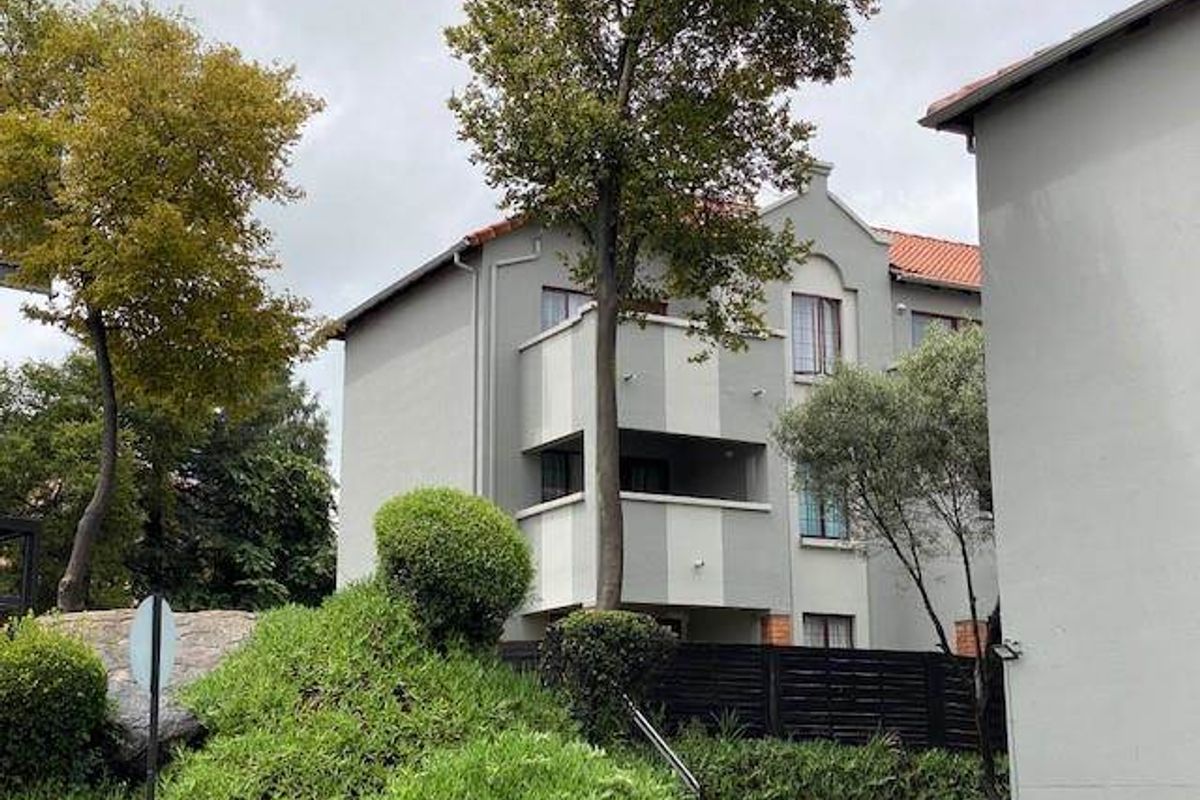 Exterior view of a multi-story apartment building featuring balconies, tiled roofing, and landscaped garden surroundings.