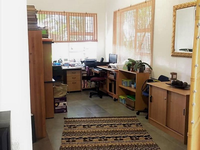 A functional home office space featuring tiled flooring and large windows with fitted blinds, providing ample natural light.