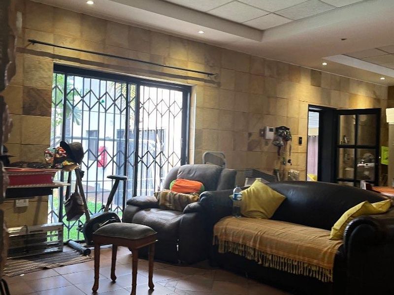 Living room featuring a stone-clad wall, tiled flooring, and a drop ceiling with recessed lighting, leading to an outdoor area via a sliding door.