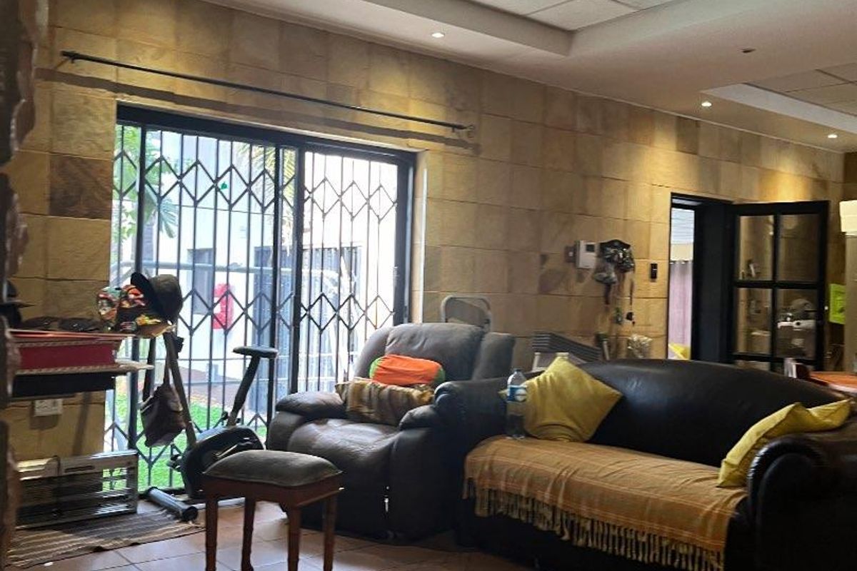 Living room featuring a stone-clad wall, tiled flooring, and a drop ceiling with recessed lighting, leading to an outdoor area via a sliding door.