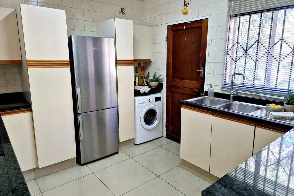 Functional kitchen featuring granite countertops, double bowl sink, tiled splashbacks, and built-in cabinetry with integrated space for laundry appliances.