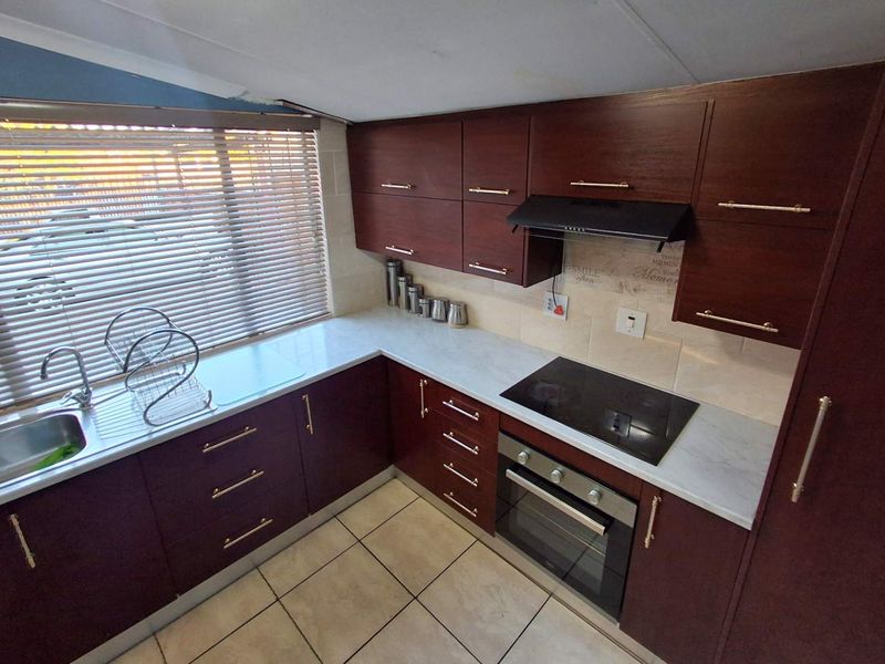 A compact kitchen featuring dark wood cabinetry, light countertops, integrated electric hob and oven, and tiled flooring.