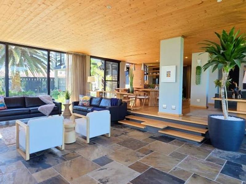 Spacious open-plan living area featuring a warm timber-clad ceiling, natural stone flooring, and expansive floor-to-ceiling glass doors that provide seamless indoor-outdoor flow.