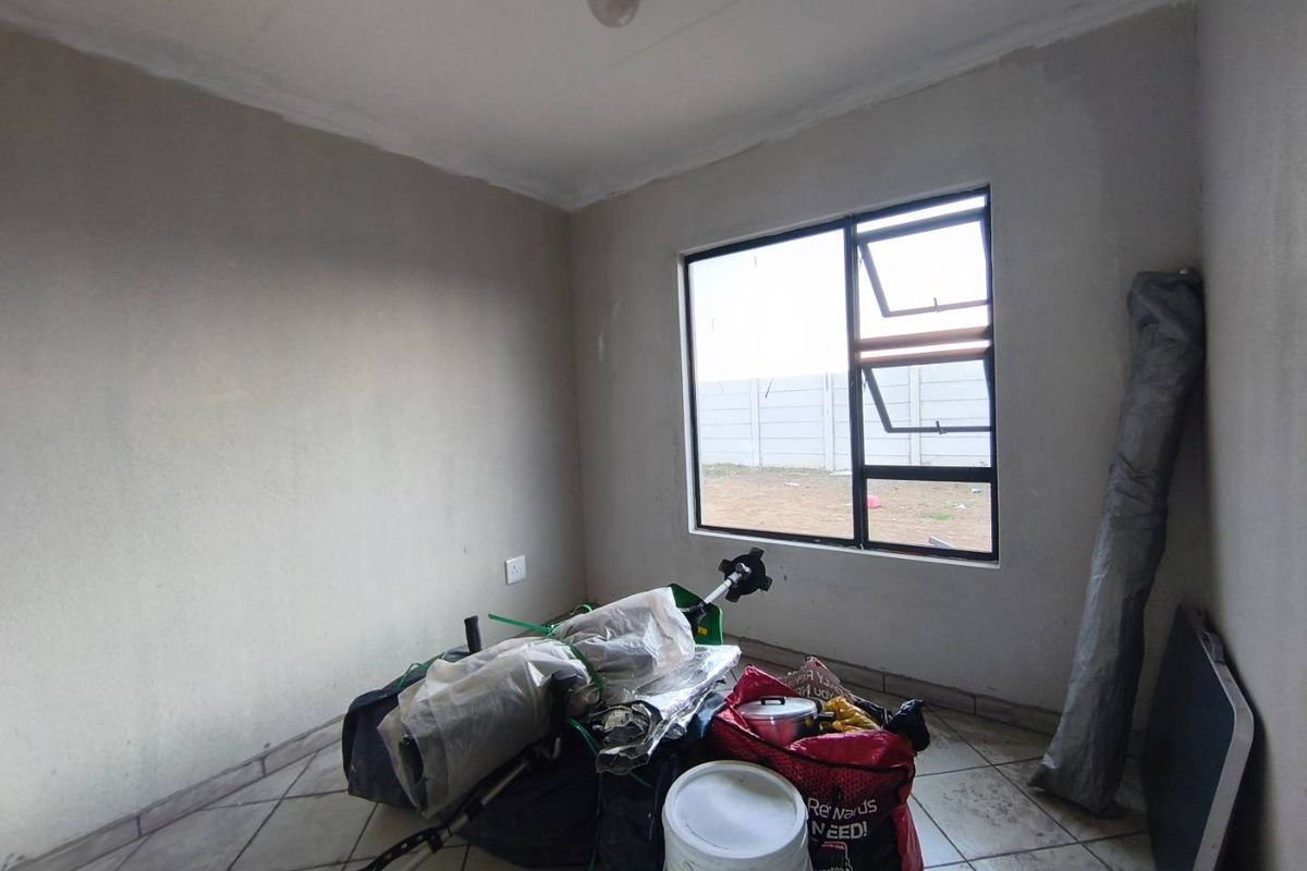 A vacant bedroom featuring tiled flooring and an aluminium window frame, presenting a blank canvas ready for renovation or staging.