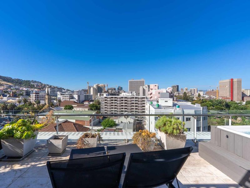 Spacious penthouse balcony featuring a glass balustrade, tiled flooring, and a built-in hot tub with panoramic city views.