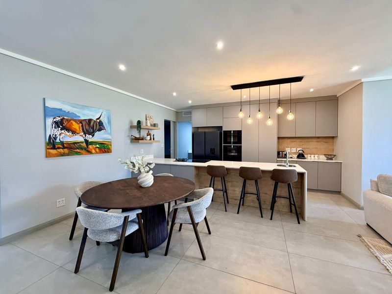 Modern open-plan kitchen and dining area featuring sleek cabinetry, a central island with breakfast bar seating, and contemporary pendant lighting.