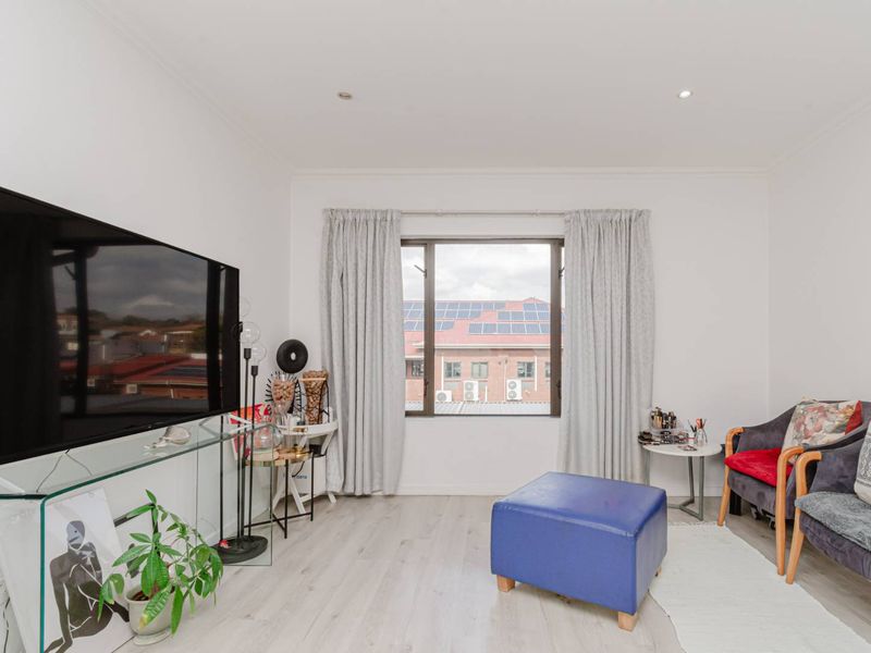 A bright living room featuring light-toned laminate flooring, recessed downlighting, and a window with views of the surrounding neighborhood.