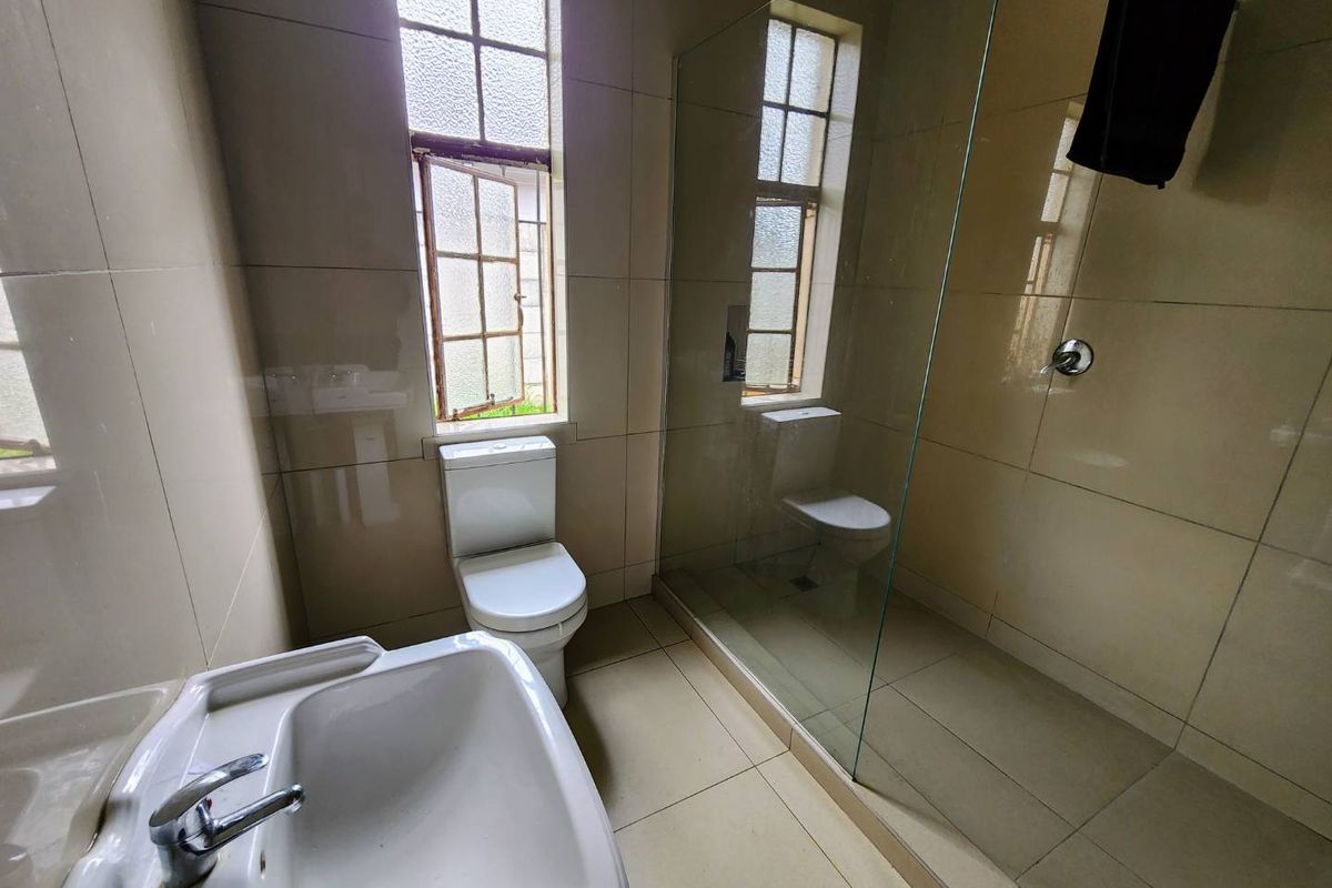 A functional bathroom featuring a glass-enclosed shower, a pedestal basin, and a toilet, finished with neutral wall and floor tiling.