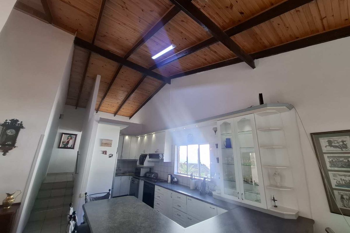 A kitchen featuring white cabinetry, dark countertops, and a vaulted timber-beamed ceiling, providing a spacious and character-filled cooking area.