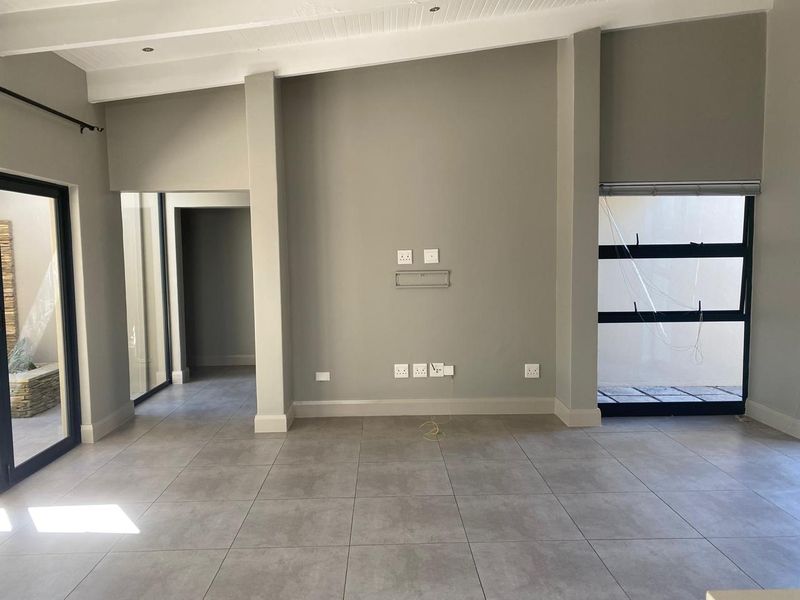 A bright, empty living room featuring neutral grey floor tiles, modern aluminium window frames, and recessed ceiling lighting, ready for personalization.