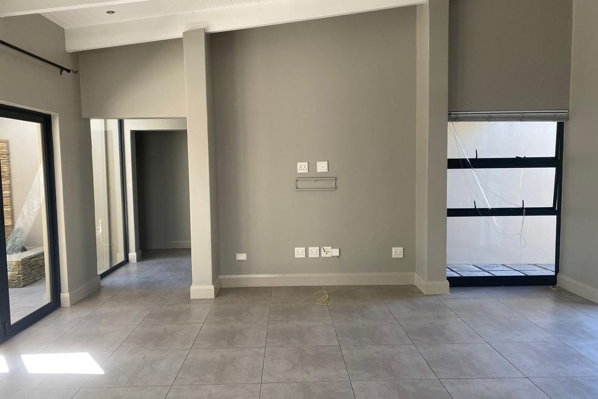 A bright, empty living room featuring neutral grey floor tiles, modern aluminium window frames, and recessed ceiling lighting, ready for personalization.