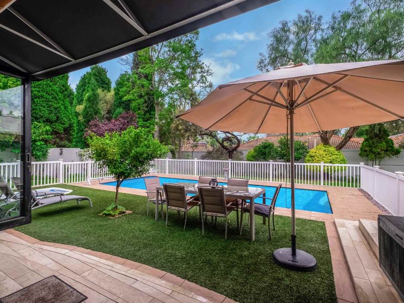 Outdoor entertainment area featuring a swimming pool, artificial lawn, tiled patio, and a retractable awning, enclosed by a white picket fence.