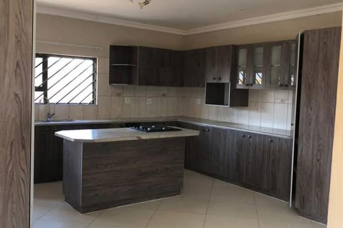 A spacious kitchen featuring dark wood-grain cabinetry, a central island with a built-in cooktop, tiled flooring, and a tiled backsplash.
