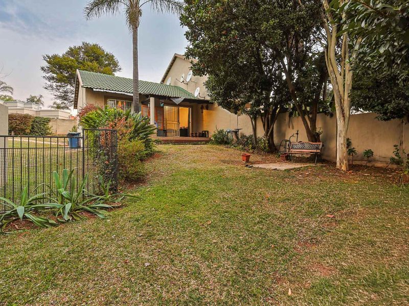 A private rear garden featuring a lawn, mature trees, boundary walls, and a small paved patio area attached to the main dwelling.