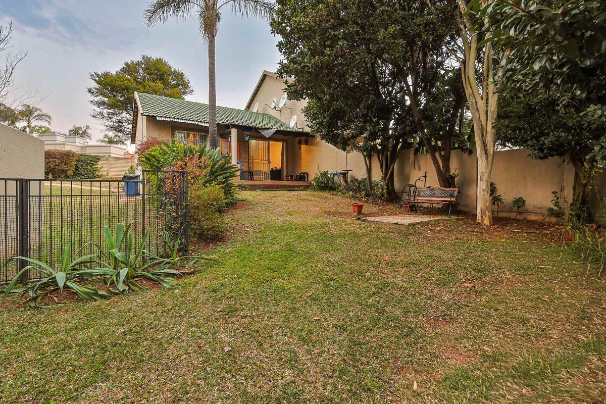 A private rear garden featuring a lawn, mature trees, boundary walls, and a small paved patio area attached to the main dwelling.