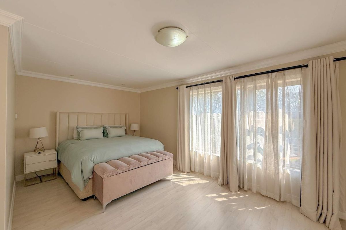 A well-maintained bedroom featuring light-toned laminate flooring, neutral wall finishes, and large windows with floor-to-ceiling curtains allowing for ample natural light.