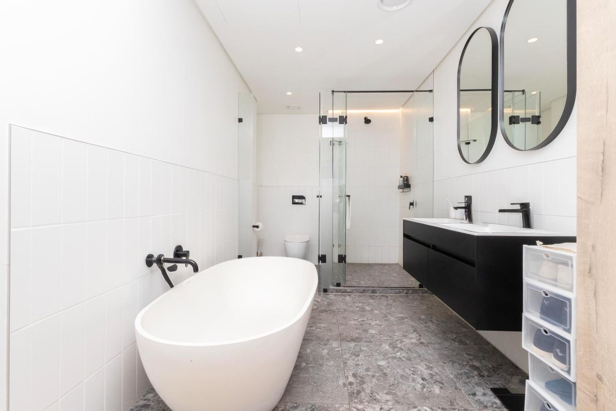 Modern bathroom featuring a freestanding bathtub, a walk-in glass shower, and a sleek double vanity with matte black fixtures and stone-look floor tiles.