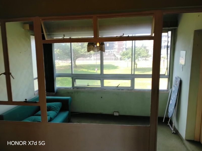 A living area featuring large windows with natural light, requiring cosmetic updates to the wall finishes and general maintenance.