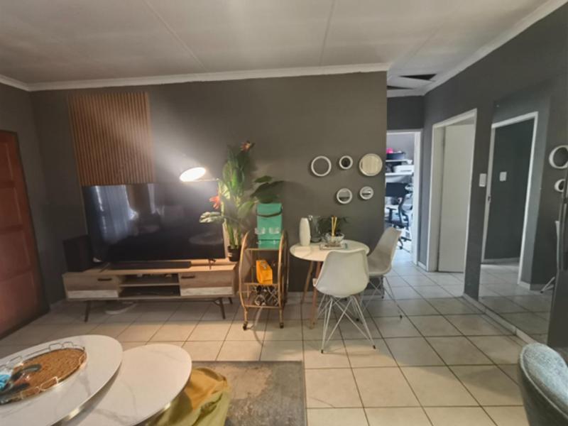 A living area featuring tiled flooring, decorative slatted wood wall paneling, and a full-length wall mirror, with visible ceiling damage requiring repair.