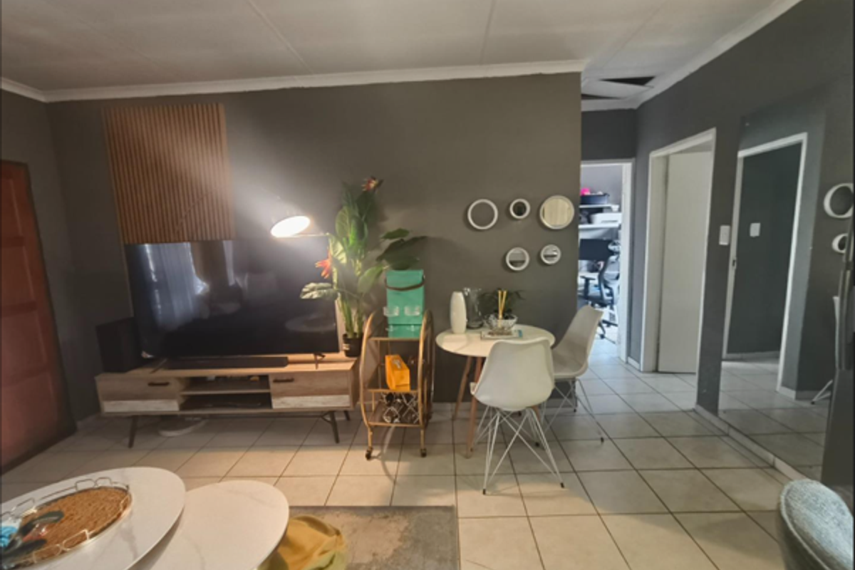 A living area featuring tiled flooring, decorative slatted wood wall paneling, and a full-length wall mirror, with visible ceiling damage requiring repair.