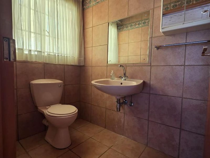 A functional bathroom featuring tiled walls and flooring, a wall-mounted basin, and a timber ceiling, offering a dated but well-maintained space.