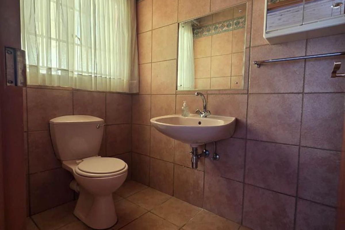 A functional bathroom featuring tiled walls and flooring, a wall-mounted basin, and a timber ceiling, offering a dated but well-maintained space.