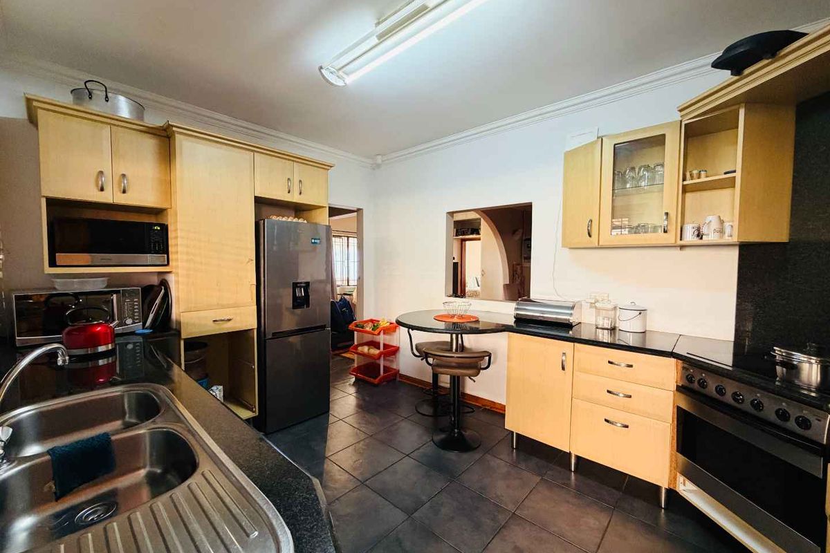 A functional kitchen featuring light wood cabinetry, dark granite countertops, a built-in oven with hob, and a double stainless steel sink.