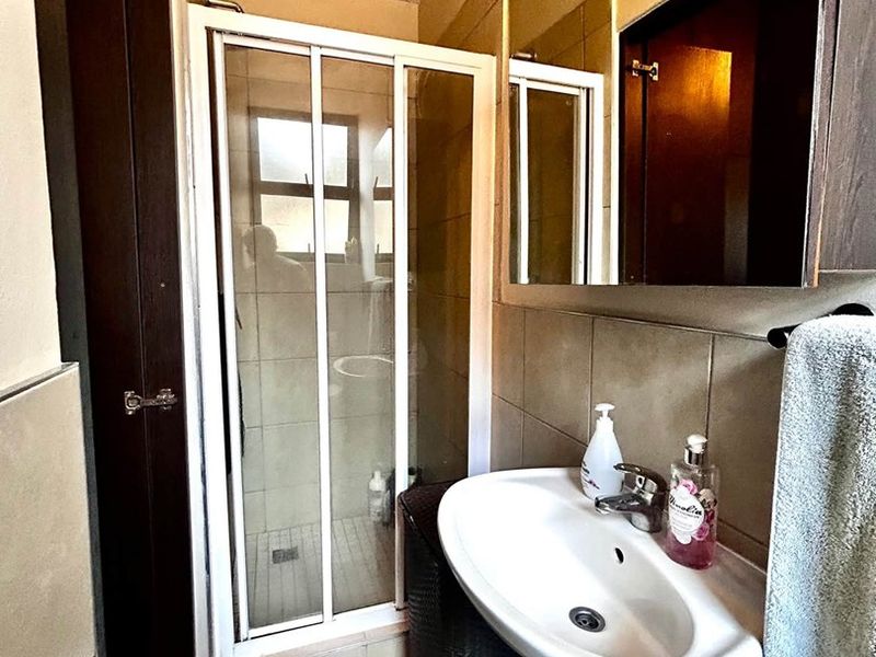 Compact bathroom featuring a shower enclosure, wall-mounted basin with mixer tap, and large wall mirror with neutral tiled finishes.