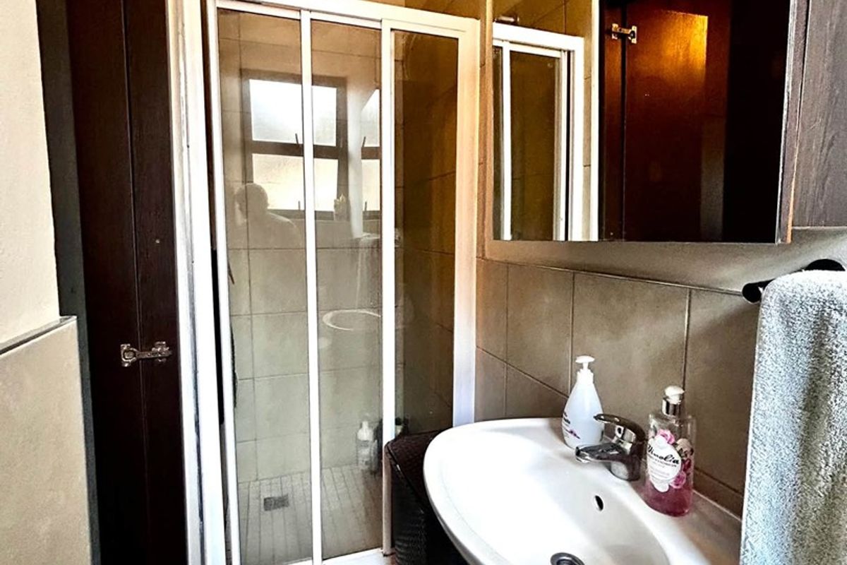 Compact bathroom featuring a shower enclosure, wall-mounted basin with mixer tap, and large wall mirror with neutral tiled finishes.