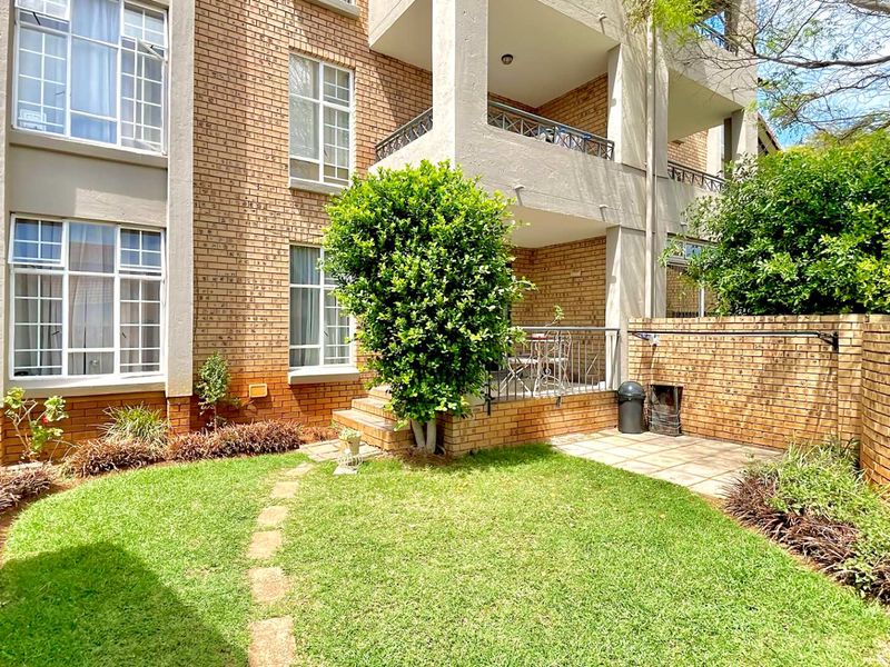Rear view of the townhouse featuring a private garden, paved patio area, and a balcony with metal railings.
