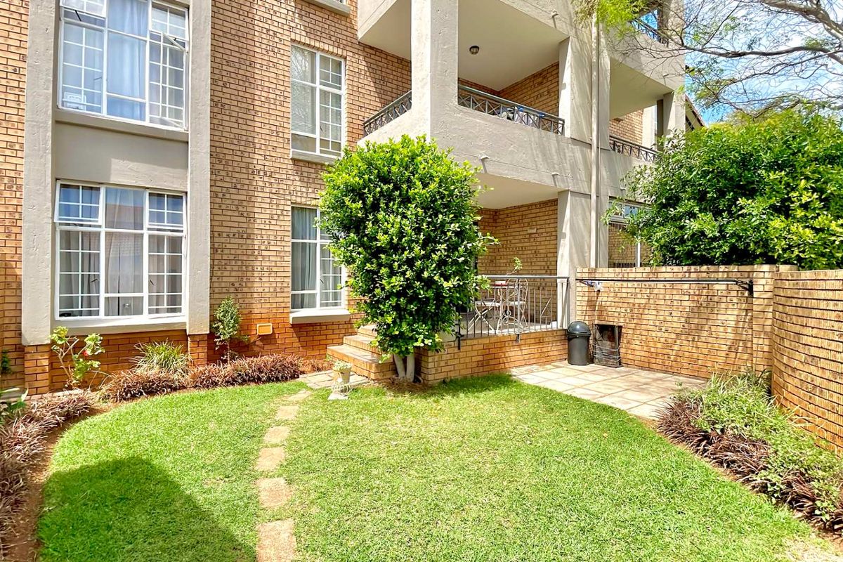 Rear view of the townhouse featuring a private garden, paved patio area, and a balcony with metal railings.