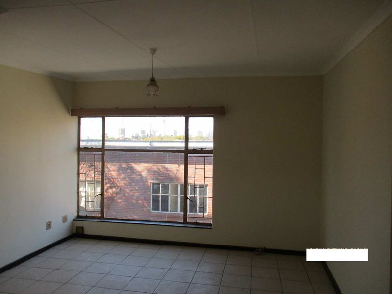 An empty bedroom featuring tiled flooring, a large window with natural light, and a simple ceiling light fixture.