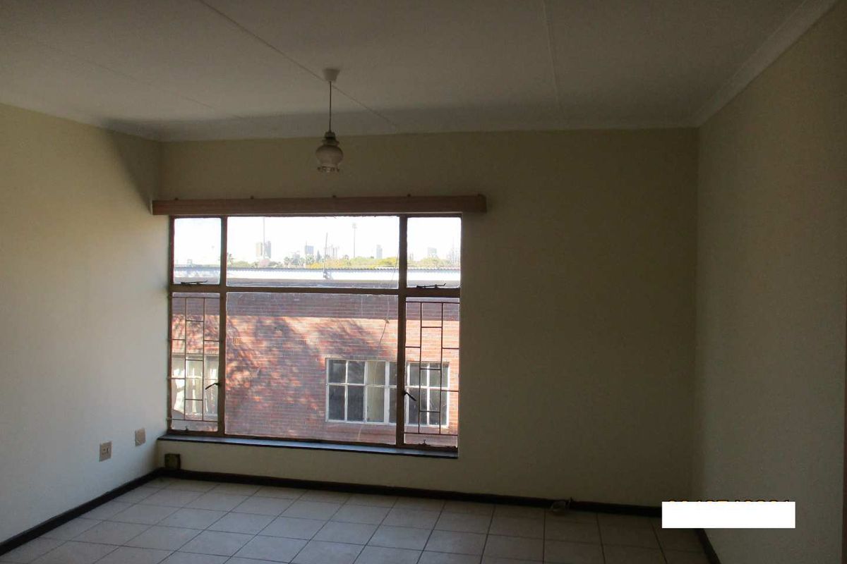 An empty bedroom featuring tiled flooring, a large window with natural light, and a simple ceiling light fixture.