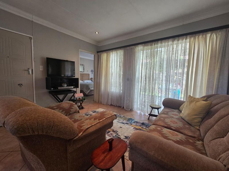 A comfortable living room featuring tiled flooring, cove cornicing, and a large sliding glass door that provides natural light and access to the garden.