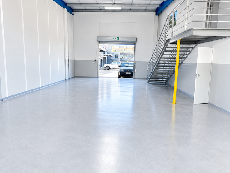 Spacious industrial utility area featuring durable epoxy flooring, a metal staircase leading to a mezzanine level, and a large roller shutter door.