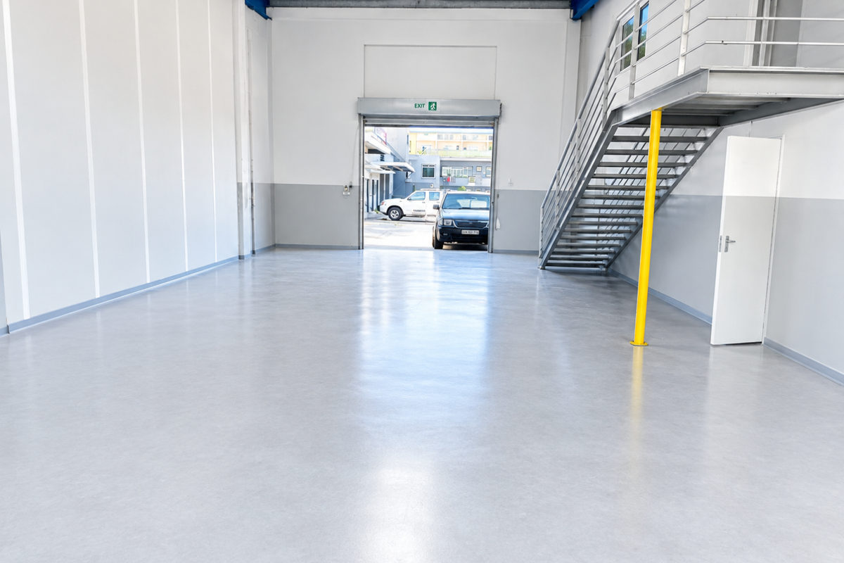 Spacious industrial utility area featuring durable epoxy flooring, a metal staircase leading to a mezzanine level, and a large roller shutter door.