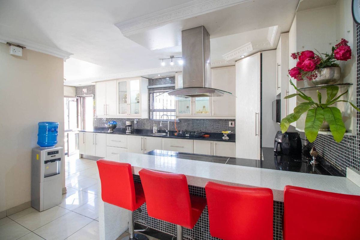 Modern kitchen featuring a breakfast bar, granite countertops, mosaic tile backsplash, stainless steel extractor fan, and ample cabinetry.