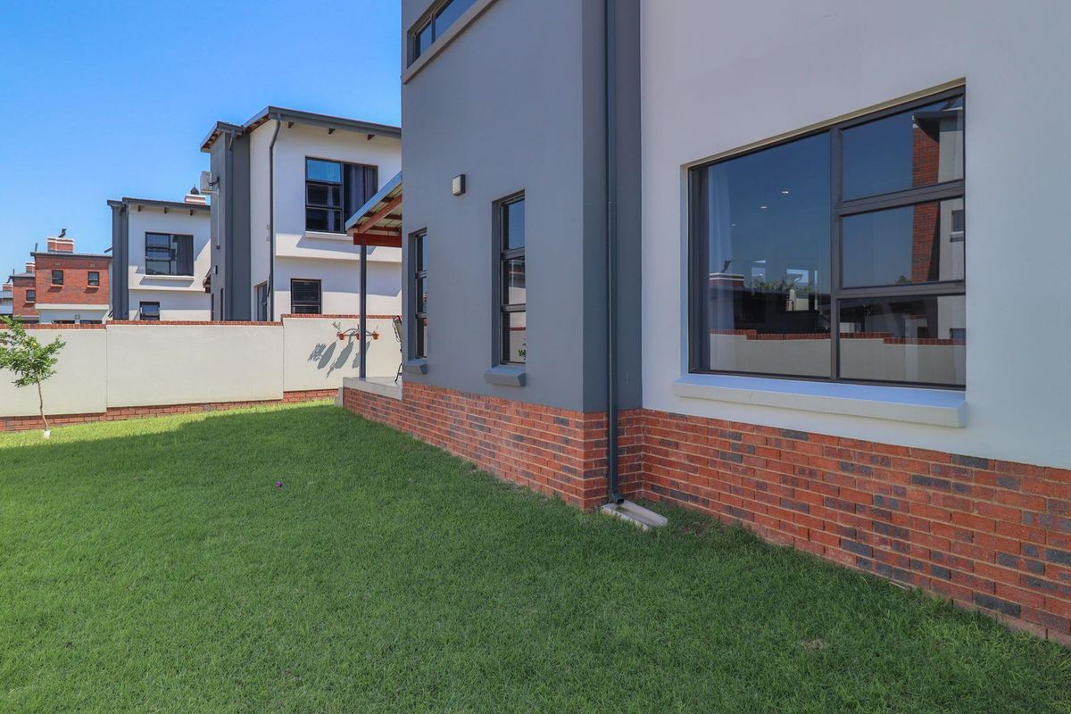 A view of the rear exterior of the house featuring a well-maintained lawn, brick base detailing, and modern aluminium window frames.