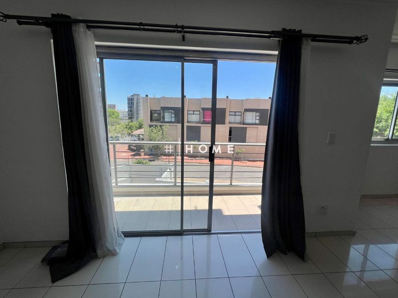A bright living area featuring a sliding glass door that opens onto a private balcony with urban views.