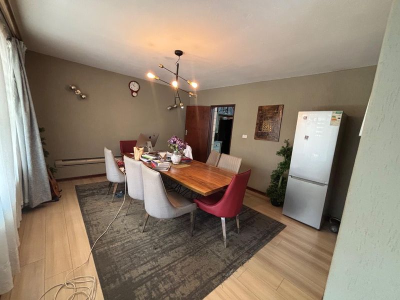 A dining room featuring light-toned laminate flooring and a modern multi-arm chandelier, providing a functional space for meals and gatherings.