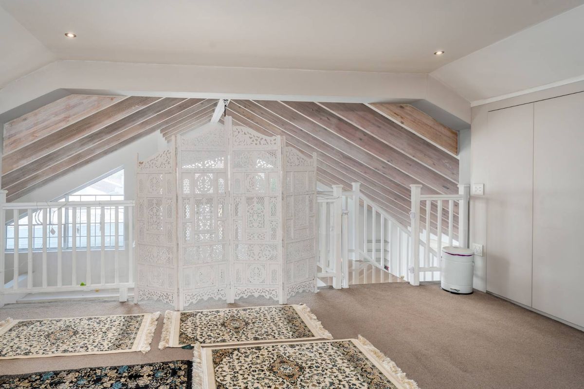 An attic-style bedroom featuring exposed timber rafters, built-in storage, and a mezzanine-style layout with white balustrades.